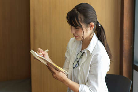 Side view of young female student looking on her notebook while doing assignment in libraryの写真素材