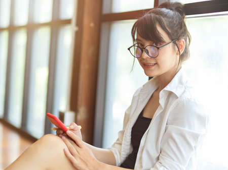 Portrait of female student smiling to camera while relaxing with smartphone in living roomの写真素材