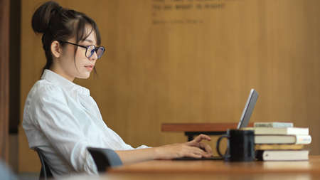 Side view portrait of young female student doing her project with digital tablet and books in...