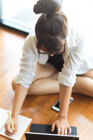 Top view of young female student doing home work with notebook and digital tablet on the floor in living roomの写真素材