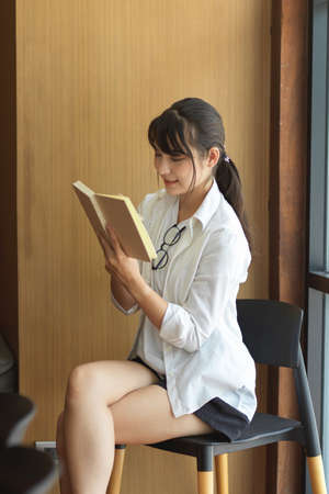 Portrait of young female student reading on her lecture book while doing assignment in libraryの写真素材