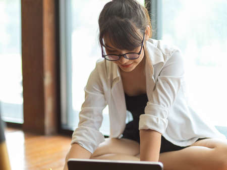 Young female student doing home work with notebook and digital tablet on the floor in living roomの写真素材