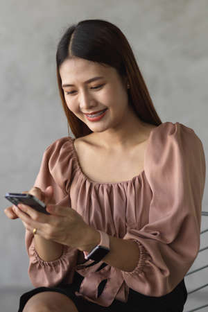 Portrait of happy female office worker texting message on smartphone while relaxed sitting in cafeの写真素材