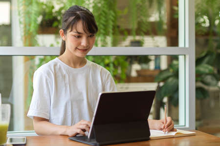 Portrait of young female student doing homework with digital tablet and stationery in home gardenの写真素材