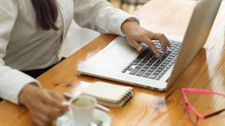 Side view of businessperson hand working with laptop and holding coffee cup on workspaceの写真素材