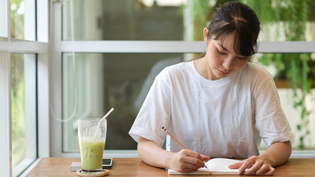 Portrait of young female teenager handwriting on her diary while relaxing in cafeの写真素材