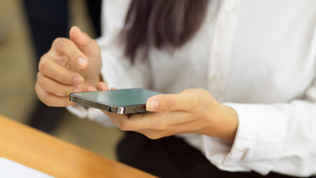 Cropped shot of female hands using smartphone, texting message on the phone in workplaceの写真素材