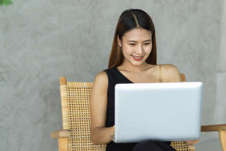 Portrait of young beautiful woman using laptop on her lap while relaxed sitting in leisure cornerの写真素材