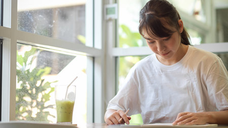 Portrait of young female student concentrating on her homework while sitting in coffee shopの写真素材