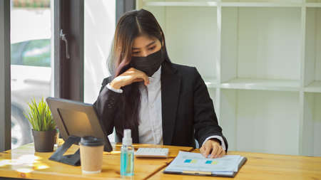 Half-length portrait of businesspeople with face mask working with digital tablet and paperwork in officeの写真素材