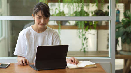 Portrait of young female student doing homework on digital tablet in cafeの写真素材