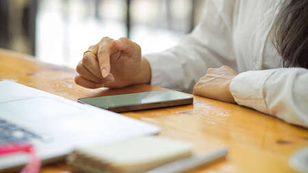 Cropped shot of female office worker working with smartphone on office deskの写真素材
