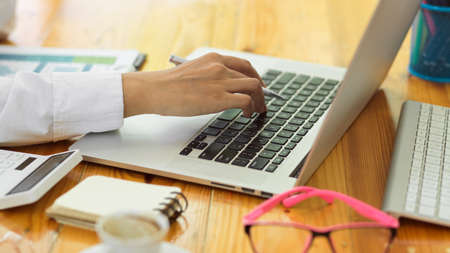 Close up view of female hands typing on laptop keyboard on wooden office desk with suppliesの写真素材