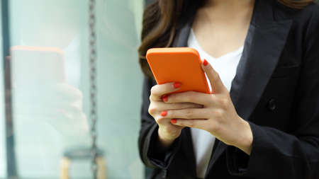 Cropped shot of businesswoman hand using smartphone while standing in office roomの写真素材