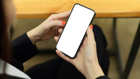 Top view of female businesswoman using smartphone with mock-up screen while siting in workplaceの写真素材