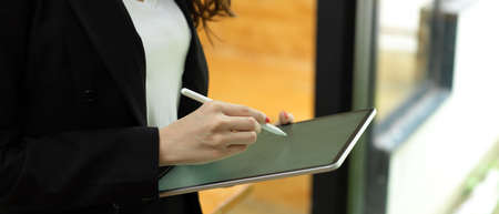 Cropped shot of businesswoman using with digital tablet while standing in office workplaceの写真素材