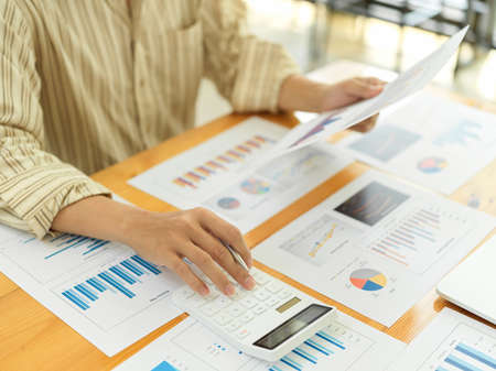Cropped shot of businessperson calculating on business documents on office deskの写真素材