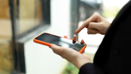 Side view of businesswoman in black suit hand using smartphone in blurred backgroundの写真素材