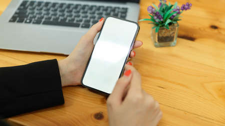 Close up view of female hands holding smartphone with mock-up screen on wooden office deskの写真素材