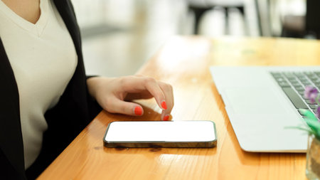 Side view of smartphone with mock-up screen on wooden desk with laptop and office workerの写真素材