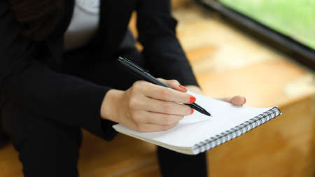 Close up view of businesswoman writing on blank notebook while sitting in relax cornerの写真素材
