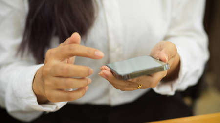 Cropped shot of female office worker using smartphone in her hands while sitting in workplaceの写真素材