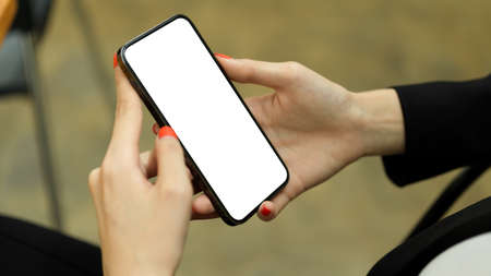Close up view of female hand holding smartphone with mock-up screen while relaxed sitting in cafeteriaの写真素材