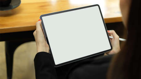 Close up view of female office worker holding digital tablet with mock-up screen while sitting in workplaceの写真素材