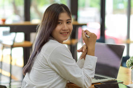 Portrait of female office worker looking back and smiling to camera while working in meeting roomの写真素材