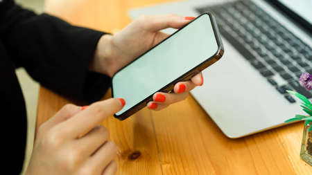 Side view of businesswoman hands using smartphone on wooden table with laptopの写真素材