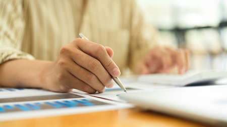 Close up view of businessperson hand with pen working with paperwork and laptop on office deskの写真素材