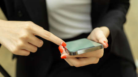Close view of businesswoman in black suit hands using smartphone, index finger touching on phone screenの写真素材