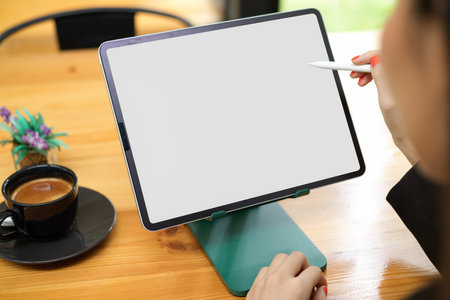 Close up view of female working on digital tablet with mock-up screen on wooden table in cafeの写真素材