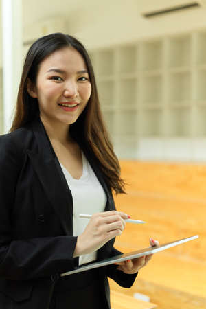 Portrait of businesswoman smiling to camera while standing and using digital tablet in office buildingの写真素材