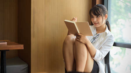 Young female student reading to prepare for upcoming exam with her lecture notebook in libraryの写真素材