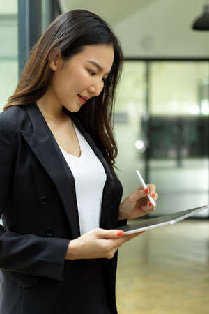 Side view of businesswoman working on digital tablet while standing in meeting roomの写真素材
