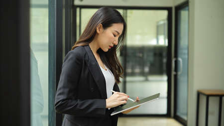 Side view portrait of businesswoman using digital tablet while relaxing in office buildingの写真素材