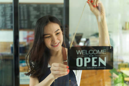 Portrait of young female barista decorating her coffee shop with the label on glass doorの写真素材