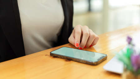 Close up view of businesswoman hand using smartphone on wooden table in office roomの写真素材