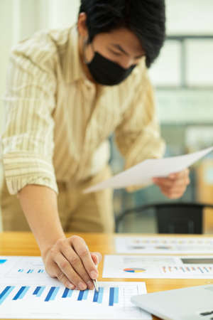 Cropped shot of businessman with face mask working on paperwork and digital tabletの写真素材