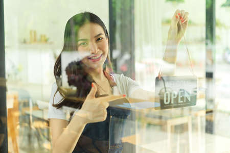 Portrait of young happy female barista decorating her coffee shop with the label on glass doorの写真素材