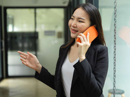 Portrait of businesswoman talking on the phone while walking in office buildingの写真素材