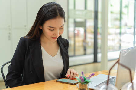 Portrait of businesswoman concentrating on her work on smartphone and laptop in office roomの写真素材