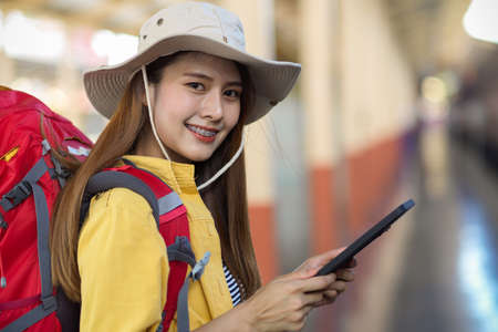 Portrait of young female backpacker smiling to camera while using digital tablet while waiting for the trainの写真素材