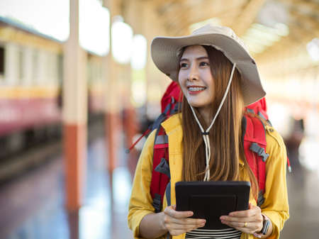 Portrait of happy young female backpacker holding digital tablet while working in platform at train stationの写真素材