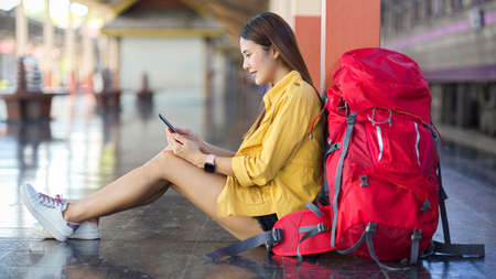Side view of female traveller using digital tablet while sitting on the floor at platform for waiting the trainの写真素材