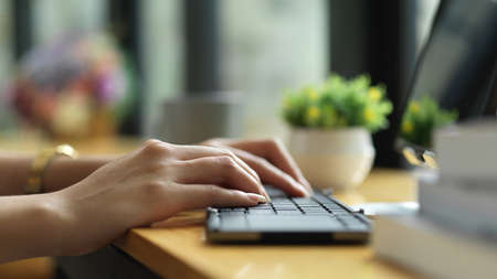 Side view of female hands typing on wireless keyboard on wooden bar in cafeの写真素材
