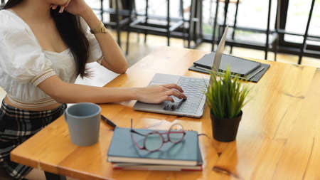 Cropped shot of female teenager doing homework with laptop and books on wooden tableの写真素材