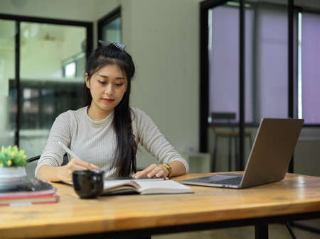 Young female student reading book to prepare for the exam in living room at homeの写真素材
