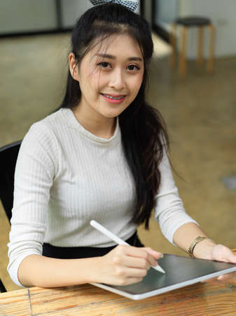 Portrait of female student smiling to camera while using digital tablet in libraryの写真素材